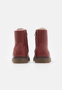 Bottines en cuir rouge avec une semelle texturée, fermeture éclair et doublure en peluche. Finition lisse avec des détails de couture visibles.