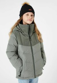 Giacca grigia imbottita con un pannello verde a coste nella parte superiore, dotata di tasche con zip e colletto alto. Indossata con un berretto in maglia nero.