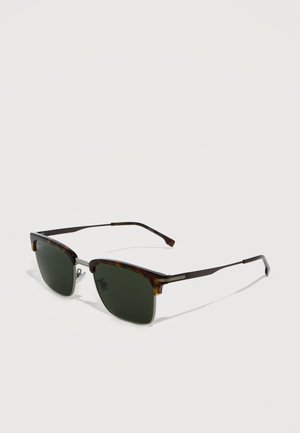 Kilpkonnakoorega ääristatud päikeseprillid tumedate ristkülikukujuliste läätsede ja õhukeste metallist sangadega, mis puhkavad heledal pinnal.