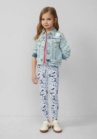 Jeansjacke mit heller Waschung, zwei Vordertaschen; pinkes T-Shirt; florale Leggings in Blau, Pink und Weiß; weiße Sneakers mit beigen Sohlen.