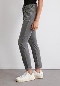 Jeans en denim gris avec une coupe slim, dotés d'une taille haute, de cinq poches et d'un design épuré, associés à des baskets blanches.