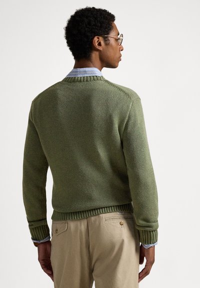 Πλεκτό πράσινο πουλόβερ με ριμπ μανσέτες και τελείωμα, φορεμένο πάνω από ανοιχτό γαλάζιο πουκάμισο με γιακά. Λείο ύφασμα και άνετη εφαρμογή.