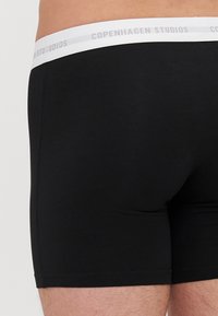 Boxeri negri dintr-o țesătură moale, cu un elastic alb la talie pe care este imprimat "Copenhagen Studios" în gri. Design simplu și croi mulat.