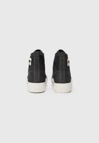 Sneakers alte in denim scuro, con suole color crema, cuciture arancioni a contrasto e un'etichetta con logo sul retro.