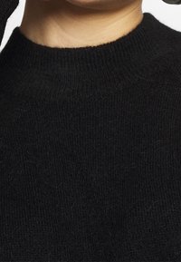 Pull noir en maille avec un col montant, présentant une finition douce et texturée ainsi que de subtiles variations dans l'épaisseur du tissu.