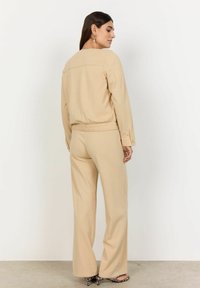 Bežová loungewear souprava, která se skládá z volného dlouhého rukávu s elastickým pasem a kalhot s širokými nohavicemi s hladkou texturou.