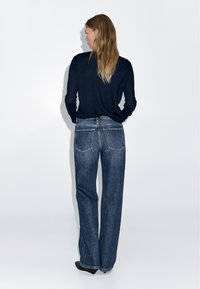 Navy long-sleeve top and high-waisted blue denim jeans. Jeans feature straight legs and two rear pockets with visible stitching.