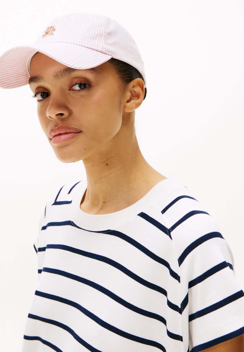 Maglietta a righe bianca con righe orizzontali blu navy; tessuto morbido; indossata sotto un cappellino a righe rosa chiaro con un logo ricamato.
