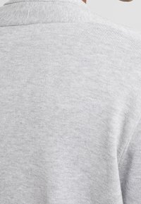 Pull gris en maille avec une texture lisse. Il présente un col rond simple et un motif subtil et uniforme sur toute sa surface.