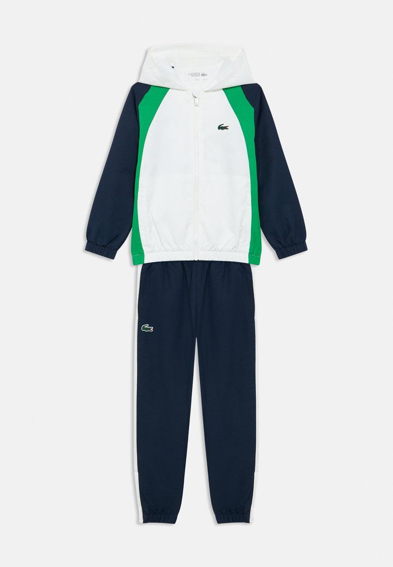 Tepláková súprava Lacoste so zapínanou mikinou na zips a kapucňou v bielej, zelenej a námorníckej modrej farbe; obsahuje elastické manžety a nohavice s logom.