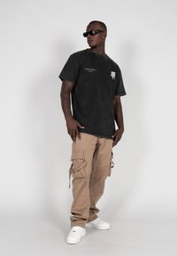 Black denim t-shirt with short sleeves, features white printed design; paired with beige cargo pants and white sneakers.
