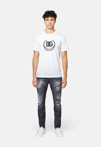 Witte katoenen T-shirt met zwart logo en laurier grafiek, gecombineerd met versleten zwarte jeans. Witte sneakers maken de outfit compleet.