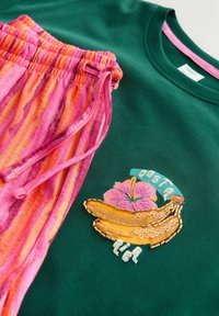 Sweat-shirt vert avec bananes brodées, fleur rose et texte « Costa Rica », associé à un pantalon à cordon rayé rose et orange.