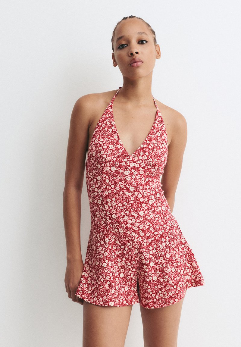 Romper floreale rosso con design a collo all' americana, caratterizzato da un corpetto aderente e pantaloni a mantello, realizzato in tessuto leggero con una consistenza morbida.