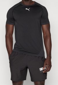 Sort atletisk skjorte med korte ærmer, strukturerede paneler og et hvidt Puma-logo. Parret med sorte shorts med et hvidt PUMA grafisk mærke.