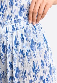 Blauwe en witte gestreepte stof met een gekreukt textuur. Elastische tailleband en bloemendesign met verschillende tinten blauwe bloemen.