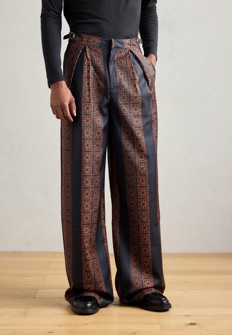 Pantalones con estampado que presentan una base azul marino con diseños geométricos en naranja, con plisado en la parte delantera y bolsillos laterales. Confeccionados en una tela suave.