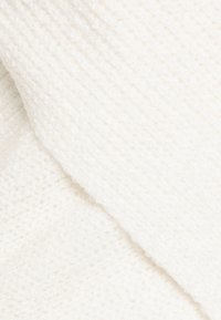 Stickad tyg i mjukt vitt med en texturerad, ribbad mönstring. Materialet verkar varmt och mysigt, med en mild lyster.