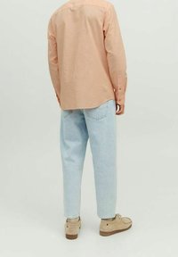 Camicia a maniche lunghe color pesco chiaro, vestibilità casual; jeans dritti blu chiaro con leggere abrasioni; scarpe beige con dettagli testurizzati.