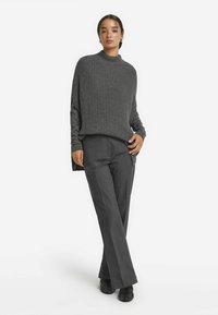 Grauer gerippter Strickpullover mit hohem Kragen. Kombiniert mit grauen, weit geschnittenen Hosen. Das Outfit zeichnet sich durch einen lässigen Schnitt und eine weiche Textur aus.