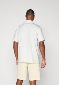 Kurzarm-Poloshirt aus hellgrauem Stoff mit dezentem Karomuster, kombiniert mit beigen Shorts, die eine reguläre Passform und weichen Stoff zeigen.