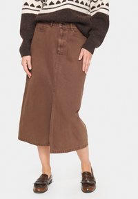 Brūns denima midi svārki ar priekšējo šķēlumu un jostu cilpām. Izgatavoti no izturīga auduma, ar kabatām un klasisku piegriezumu. Saskaņoti ar brūns loafers.