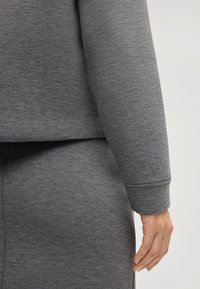Felpa grigia con un design corto, polsini a coste e texture morbida. Fa parte di un completo coordinato con pantaloni a vita elastica.