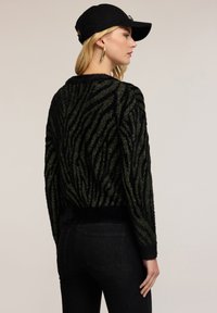 Maglione peloso a righe nere e verdi con una consistenza morbida. Presenta un orlo e polsini a costine, maniche lunghe e una vestibilità rilassata.