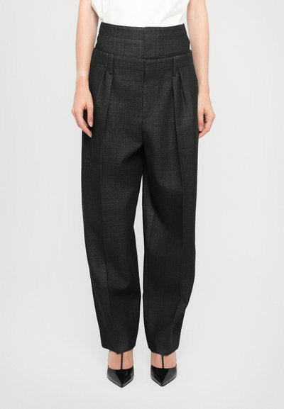 Pantalons noirs taille haute avec plis, en tissu texturé ; coupe ample se rétrécissant au niveau de la cheville. Associés à des talons aiguilles noirs.
