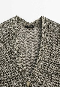 Cardigan en maille avec fil noir et blanc dans un motif texturé, présentant un col en V et une fermeture à bouton rond unique.