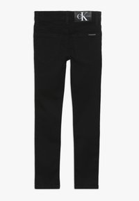 Jeans skinny de denim negro con una textura suave, que presentan un diseño clásico de cinco bolsillos y una etiqueta de marca en la parte trasera de la cinturilla.