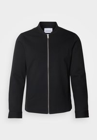 Veste bomber noire à manches longues avec fermeture éclair argentée à l'avant et petit col montant, présentée sur un fond clair uni.