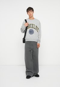 Gray sweatshirt with "BERKELEY" in yellow text and round emblem. Loose-fitting gray pants. Black shoulder bag and slip-on shoes.