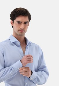 Camicia a quadri azzurro chiaro con colletto classico, maniche lunghe e polsini con bottone; il tessuto sembra liscio e leggermente strutturato.