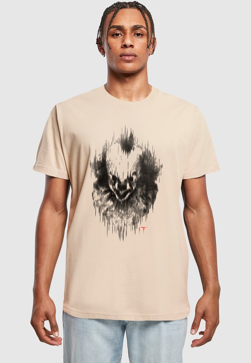 Beige Baumwoll-T-Shirt mit einem schwarzen Klangwellen-Grafikdesign und Gesicht sowie roten Akzenten. Klassischer Rundhalsausschnitt und kurze Ärmel.