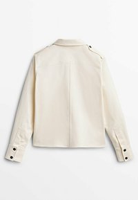 Veste à manches longues couleur crème avec un col, des épaulettes et des poignets boutonnés. Présente un design au dos épuré et un tissu texturé.