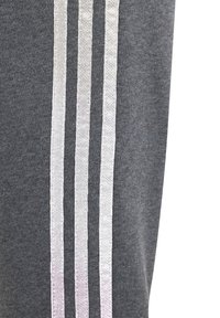 Grå sweatpants med tre vertikala silverränder längs sidan. Materialet är mjukt med en slät yta och en avslappnad design.