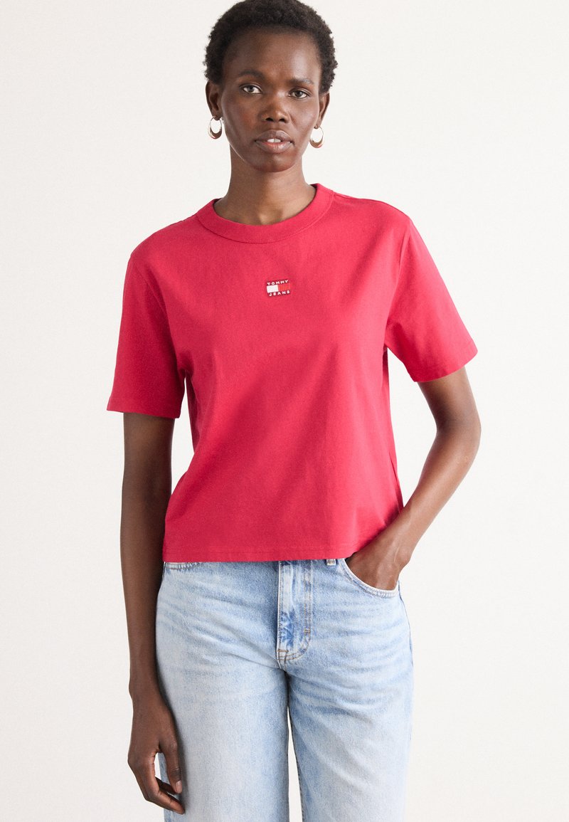Rød bomulds-T-shirt med rund hals og korte ærmer. Har et lille "TOMMY" logo på brystet. Bæres med lyseblå denim jeans.
