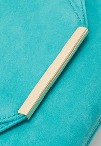 Taschen aus türkisfarbenem Wildleder mit goldenen Metallelementen. Die Oberfläche ist glatt mit feiner Textur, und entlang der Kanten befinden sich gestickte Details.