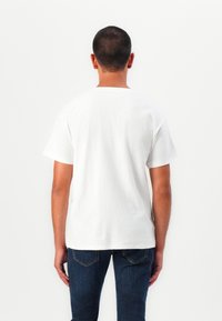 Tricou alb cu mânecă scurtă, realizat din bumbac moale, cu o croială lejeră, prezentând un guler rotund și un design minimal. Imaginea este din spate.