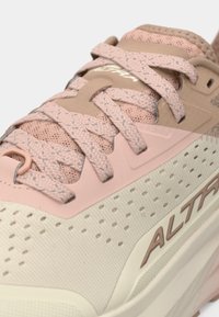 Sapatilha desportiva rosa claro com parte superior texturizada, áreas de malha e sola clara em contraste; apresenta detalhes intrincados nos atacadores e acentos de logótipo.