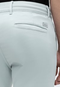 Gros plan d'une poche arrière de pantalon bleu clair sur mesure avec passants de ceinture et petite étiquette logo BOSS sur le côté droit.