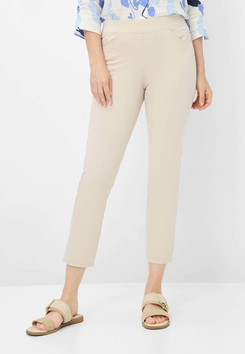 Beige slim-fit broek met een gladde textuur, voorzien van voorzakken en een middelhoge taille. Draag met lichtbruine open teen sandalen.