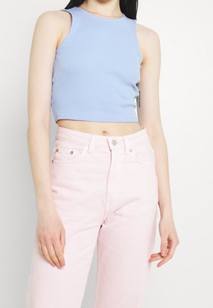 Hellblaues, geripptes Crop-Top mit rundem Ausschnitt, kombiniert mit hoch taillierter, hellrosa Jeans mit vorderen Taschen und silbernen Beschlägen.