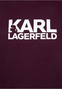 Burgunderfarbenes T-Shirt mit fettgedrucktem weißen Text "KARL LAGERFELD" und einer Silhouette-Grafik. Weicher, strukturiertes Material mit Rundhalsausschnitt.