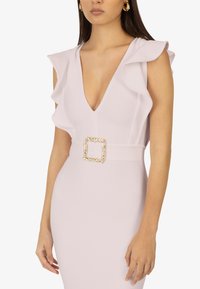 Robe ajustée rose clair avec épaules à volants, décolleté en V profond et large ceinture ornée d'une boucle carrée dorée avec motif de feuille.