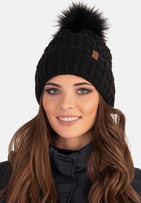 Beanie nera lavorata a maglia con motivo testurizzato, decorata con un pompon in pelliccia sintetica nera e caratterizzata da una piccola etichetta in similpelle.
