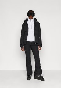 Slēpošanas apģērbs, kas ietver melnu puffer jaku, balto pamatkārtu, melnus slēpošanas bikses un melnus slēpošanas zābakus. Ietver kapuci un ar rāvējslēdzējiem aizveramas kabatas.