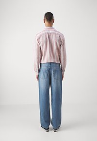 Chemise à rayures roses et blanches à manches longues, jean bleu clair ample et baskets noires. La tenue présente un design décontracté avec une coupe confortable.
