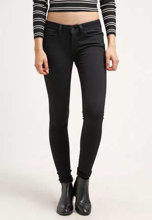 Vaqueros skinny negros con una textura suave, diseño de cinco bolsillos y bucles para cinturón, combinados con botas negras hasta el tobillo y una blusa acortada de rayas.